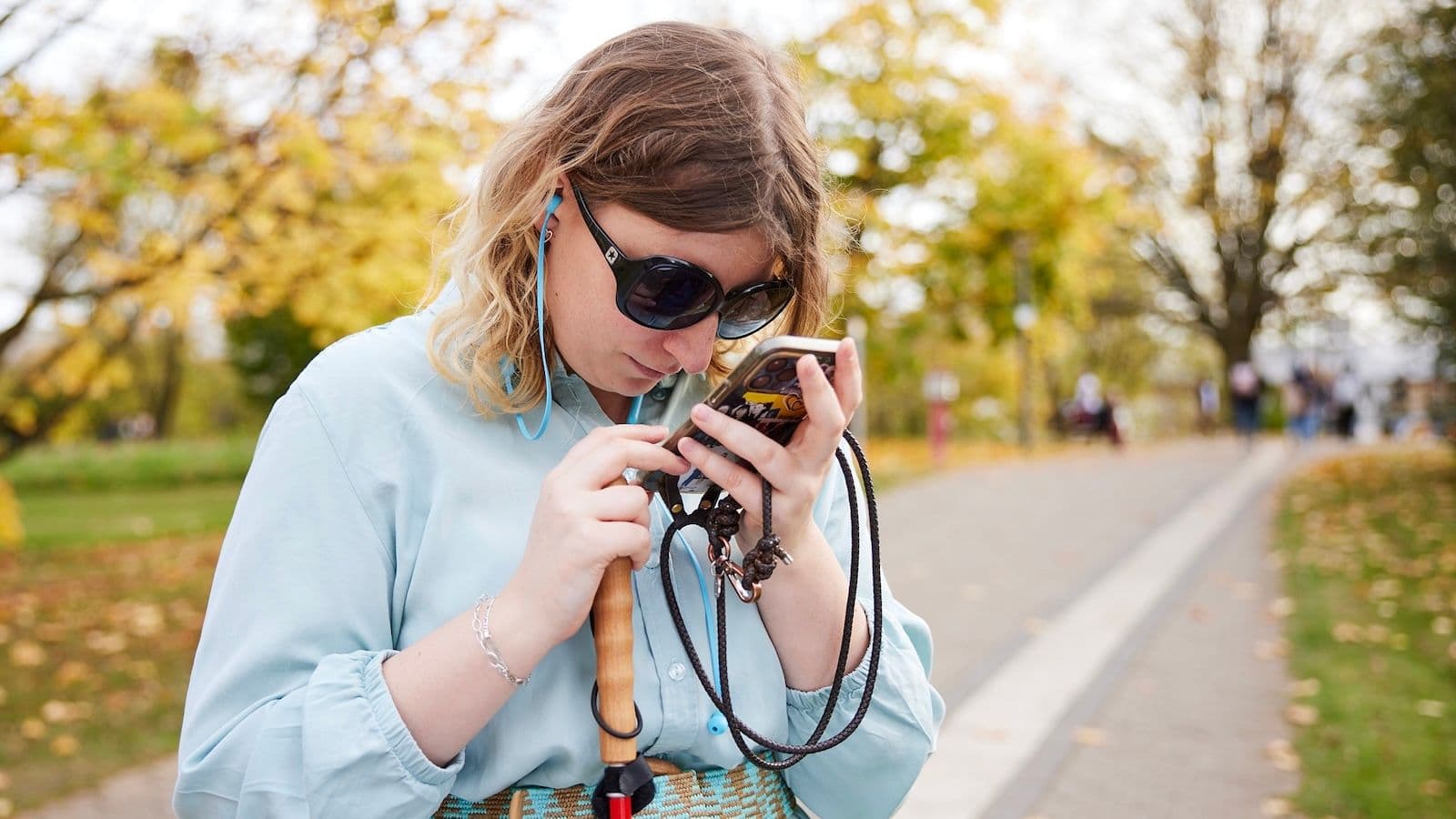 A blind woman with dark glasses holding a smartphone close to her face. Via gesellschaftsbilder.de ID 4212.