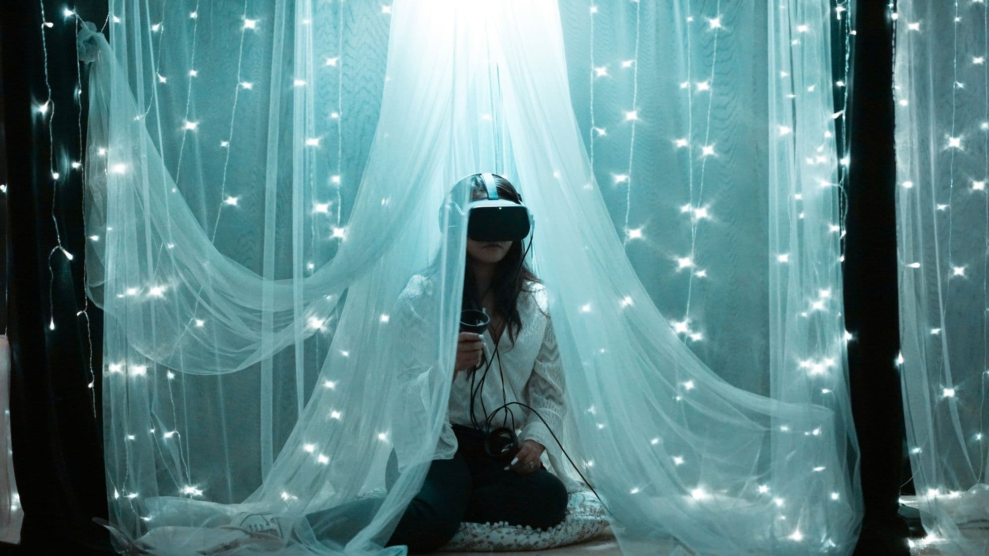 A woman with a VR headset and controllers sitting under a white sheet with lights, resembling the night sky.