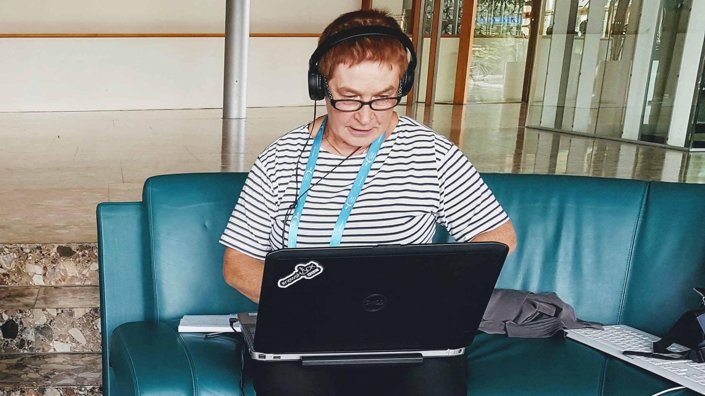 Peggy sitting on a couch, working on a laptop, and wearing headphones.