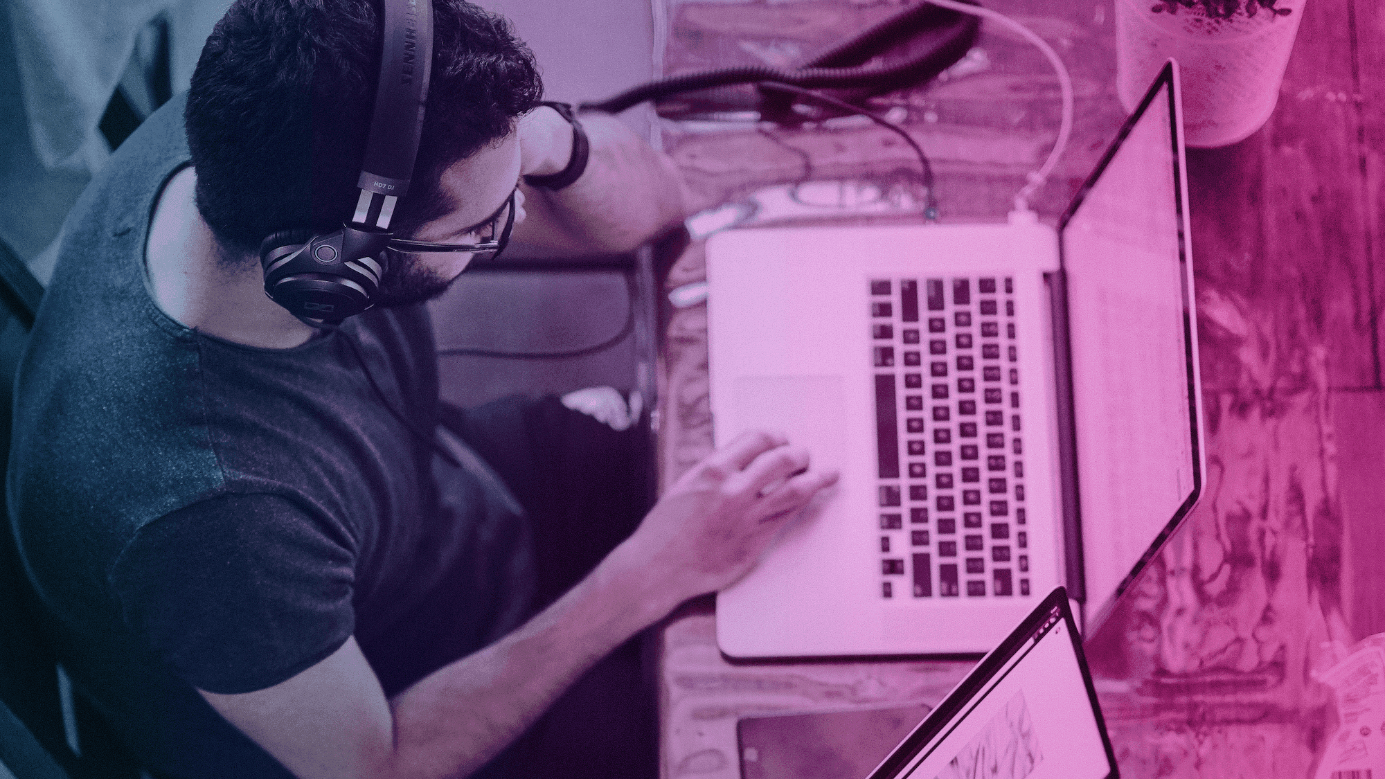 Photo shows a man wearing headphones and working on a laptop.