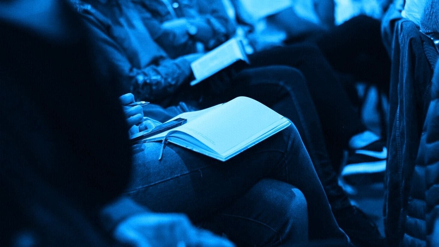 Close-up of a group of people taking notes during a conference.