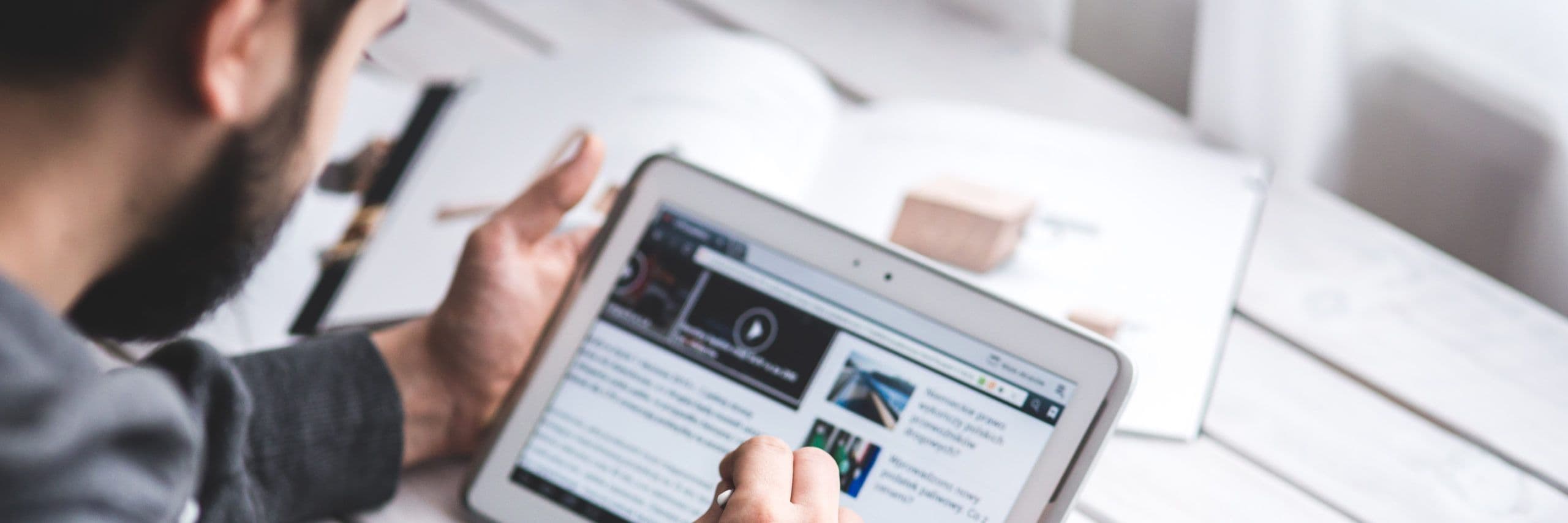 Picture shows a man watching a video and reading a text on a tablet he's holding in his hands.