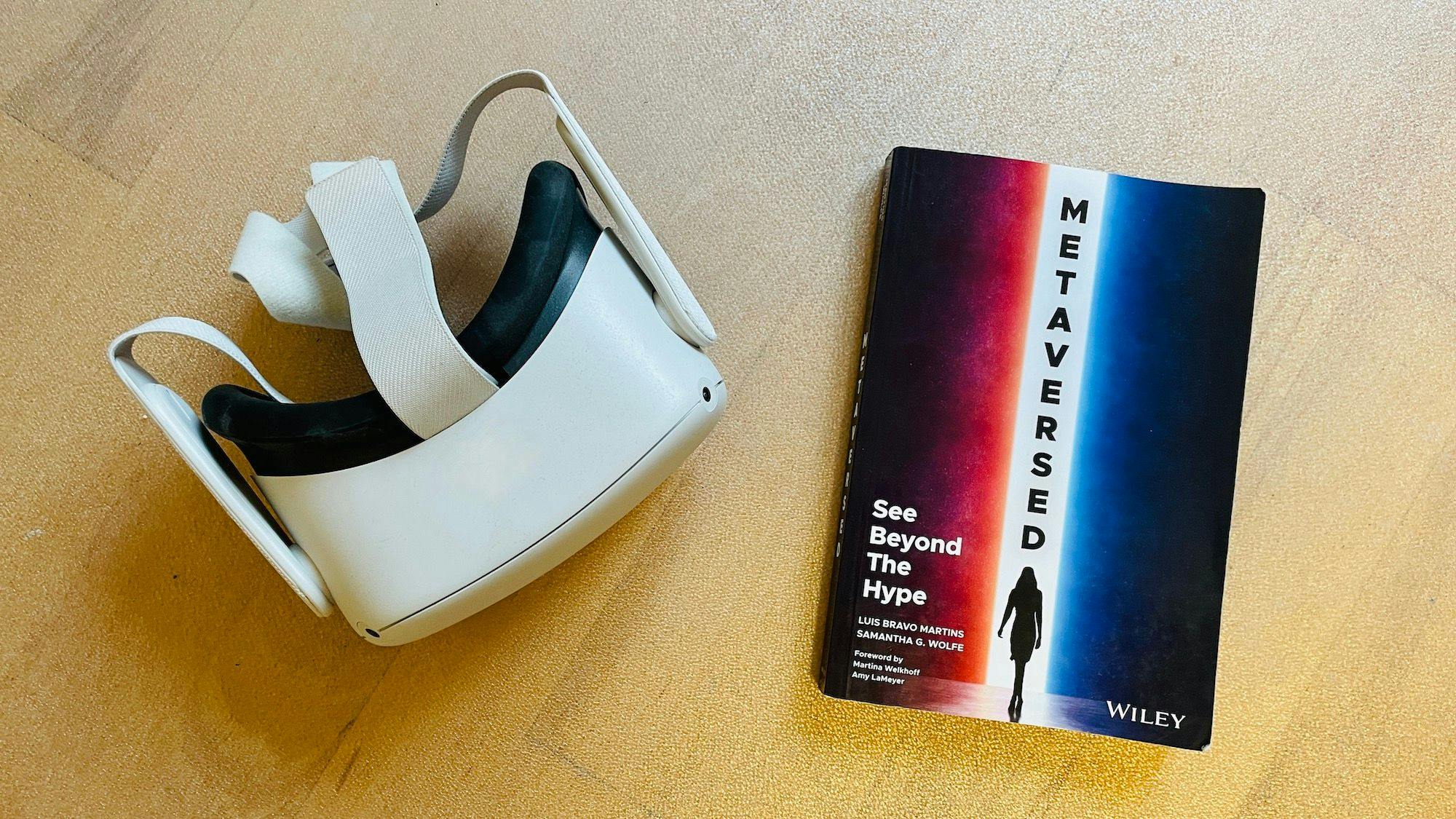 A photo of a modern XR headset next to a copy of "Metaversed"