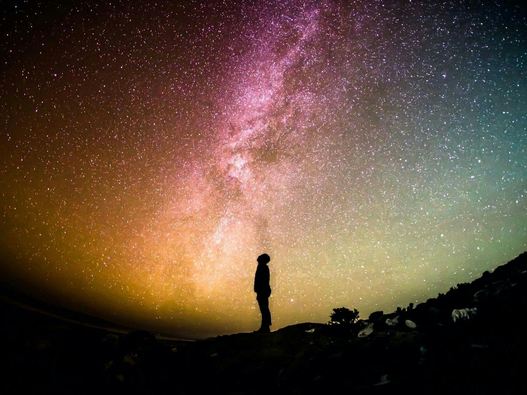 The  silhouette of a person against a colorful, starry night sky.